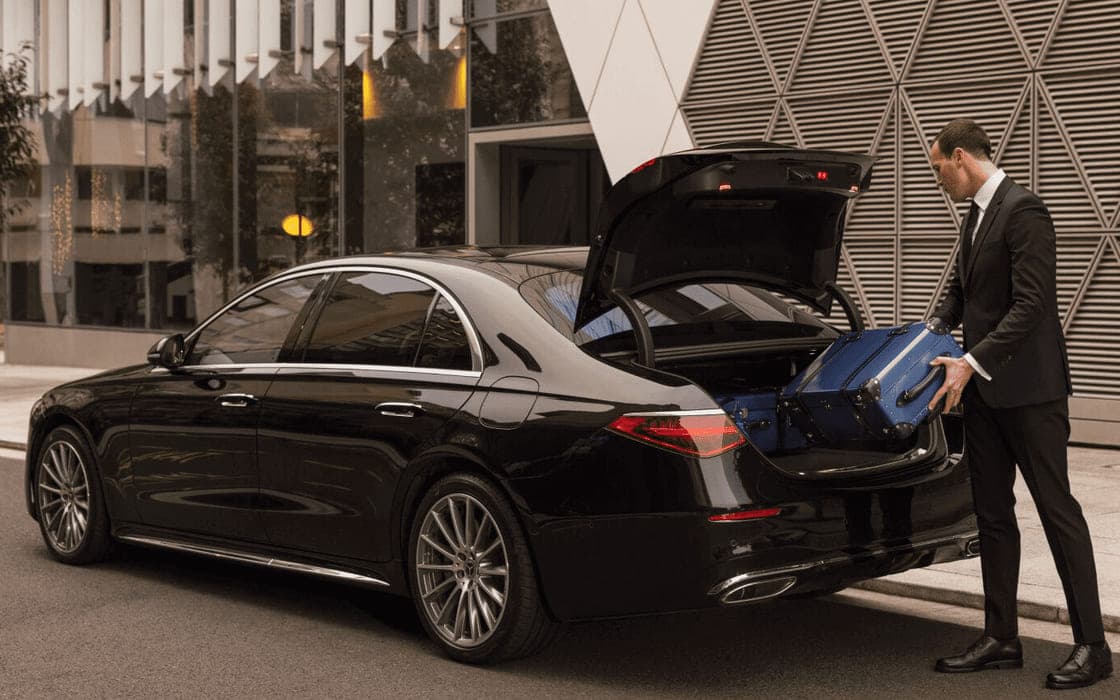 A chauffeur loading suitcases into the boot of an executive car
