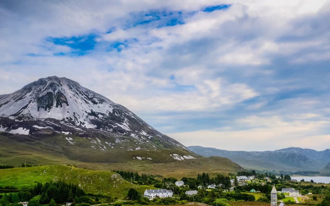 A mountain rising over green fields and a village in the west of Ireland